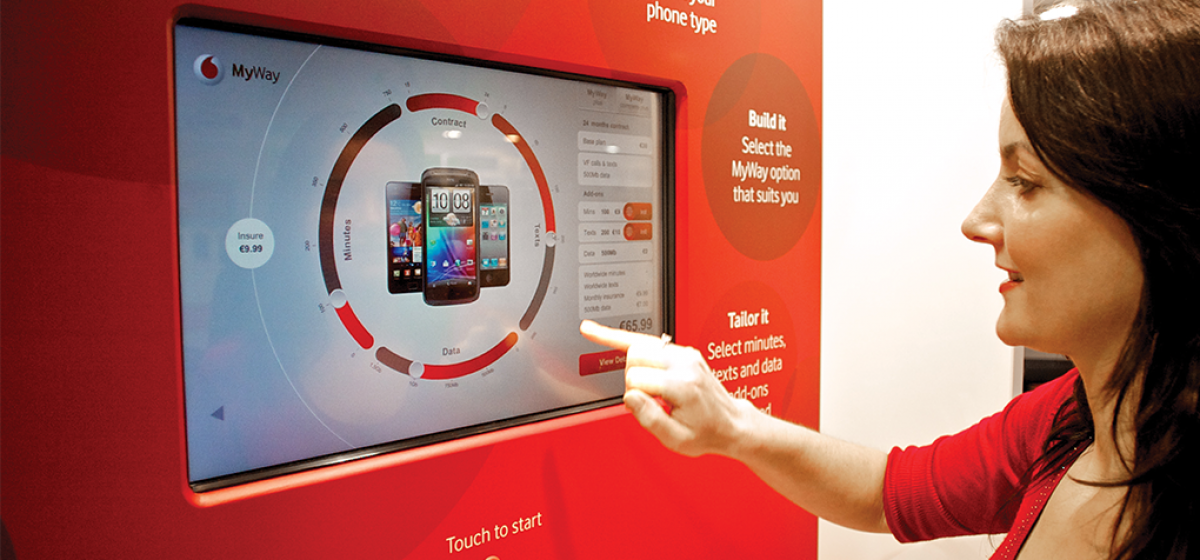 A woman using an inshore touch screen tool with mobile phones and plan details